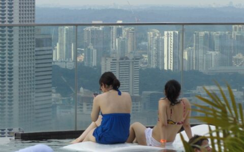 Das Handy: Der ständige ideale Begleiter - kommunikativ, aber redet nur auf Wunsch. Für viele besser als jedes Haustier. Die beiden jungen Frauen sitzen im Poolbereich des Marina Bay Sands Hotel in Singapore.