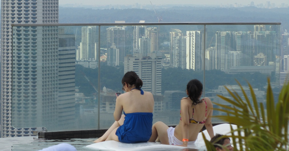 Das Handy: Der ständige ideale Begleiter - kommunikativ, aber redet nur auf Wunsch. Für viele besser als jedes Haustier. Die beiden jungen Frauen sitzen im Poolbereich des Marina Bay Sands Hotel in Singapore.