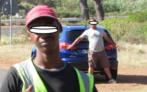 Ein Mann versucht den neuen Ford während des Drehs zum neuen Werbespots am Kap der Guten Hoffnung zu verdecken. Ein farbiger Mitarbeiter kommt auf den Fotografen drohend zu.