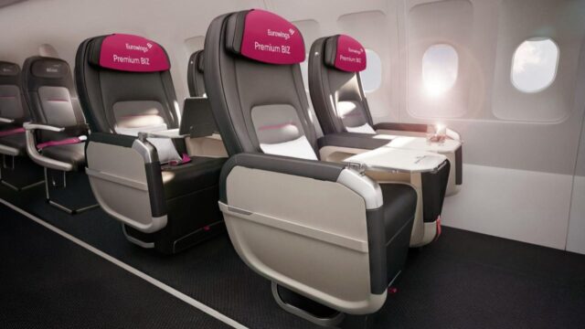 Blick in die vordere Kabine eines Eurowings-Flugzeugs mit den neuen Premium-BIZ-Sitzen in Zweierreihen, Kopfstützen mit dem Schriftzug Premium BIZ, ausgeklappten Tischen und Fenstern mit einfallendem Sonnenlicht.
