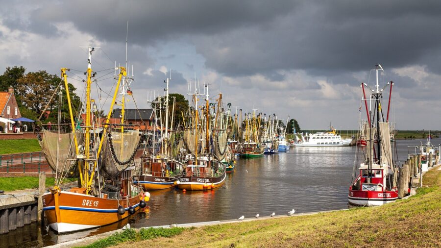 Mehrere Krabbenkutter liegen im Hafen von Greetsiel in Ostfriesland vor einem bewoelkten Himmel.