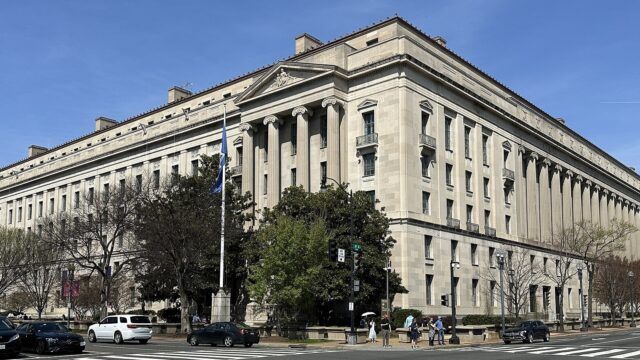 Hauptgebäude des US-Justizministeriums in Washington, ein langgestreckter Steinbau mit Säulenreihe an einer Straßenkreuzung