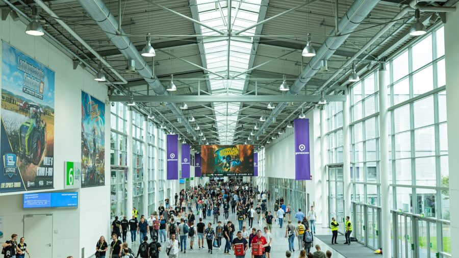 Breiter Gang einer Messehalle der gamescom in Köln mit Besuchern, Deckenfenstern und Bannern der Messe