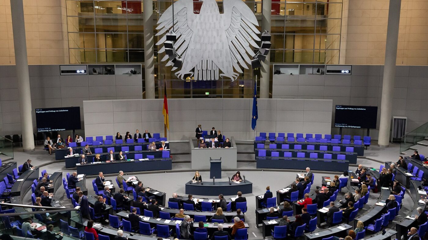 Blick von oben in den Plenarsaal des Deutschen Bundestages mit blauen Sitzreihen, Rednerpult und Bundesadler.