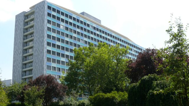 Das Hauptgebäude des Statistischen Bundesamtes in Wiesbaden, ein langgestreckter Hochbau mit blau-grauer Rasterfassade, dahinter Bäume