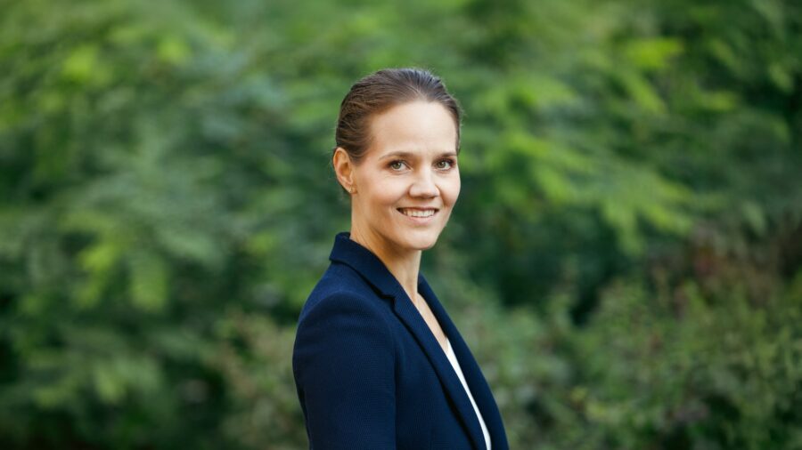 Porträt von Barbara Metz, Bundesgeschäftsführerin der Deutschen Umwelthilfe, im dunklen Blazer vor grünem Laub.