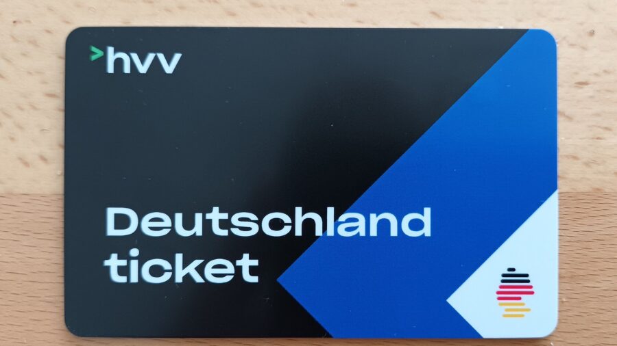 Schwarz-blaue Chipkarte mit der Aufschrift Deutschlandticket und dem Logo des Hamburger Verkehrsverbundes, liegend auf einer hellen Holzfläche