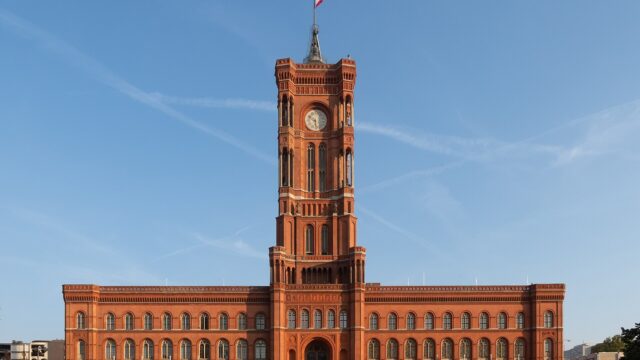 Das Rote Rathaus in Berlin bei Sonnenschein, Frontansicht der roten Backsteinfassade mit dem Uhrturm in der Mitte.
