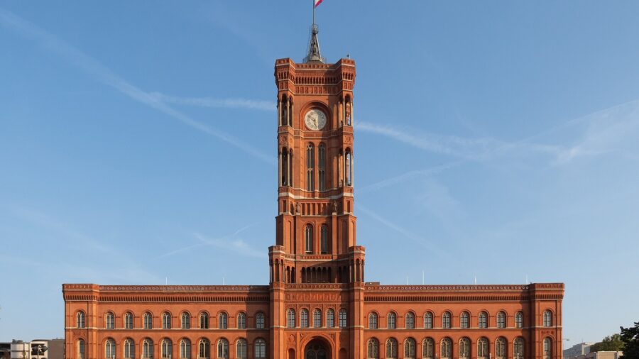 Das Rote Rathaus in Berlin bei Sonnenschein, Frontansicht der roten Backsteinfassade mit dem Uhrturm in der Mitte.