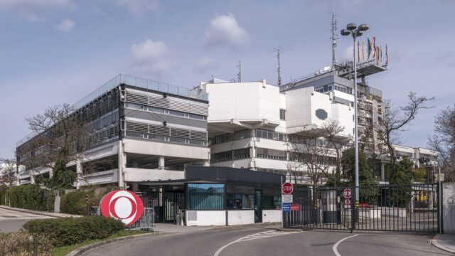 Eingangsbereich des ORF-Zentrums am Küniglberg in Wien mit dem roten ORF-Logo am Tor und Fahnenmasten vor dem Sendegebäude