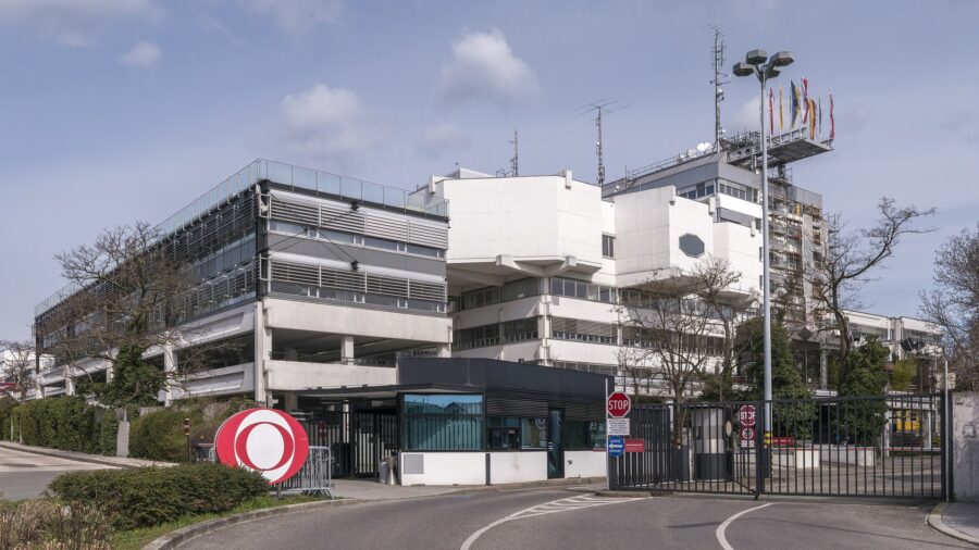 Eingangsbereich des ORF-Zentrums am Küniglberg in Wien mit dem roten ORF-Logo am Tor und Fahnenmasten vor dem Sendegebäude