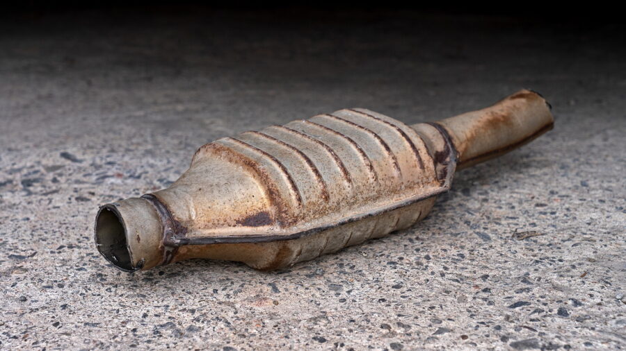 Ein ausgebauter, verrusster Fahrzeugkatalysator aus Metall liegt auf einer Betonflaeche. Das Gehaeuse ist gerippt, an einem Ende ist das Anschlussrohr abgetrennt.