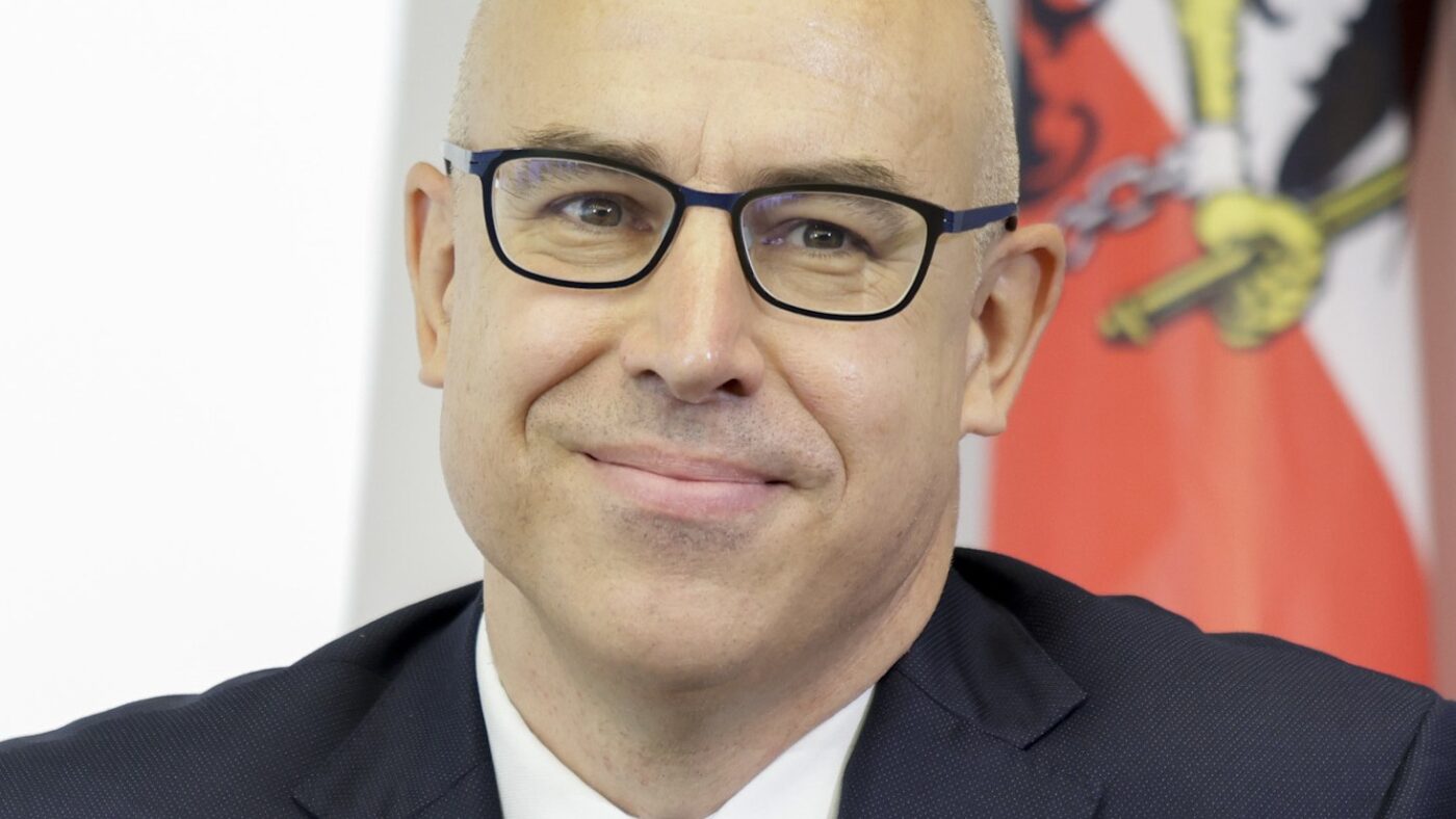 Gabriel Felbermayr, Direktor des österreichischen Wirtschaftsforschungsinstituts Wifo, im dunklen Anzug mit Brille vor einer österreichischen Fahne