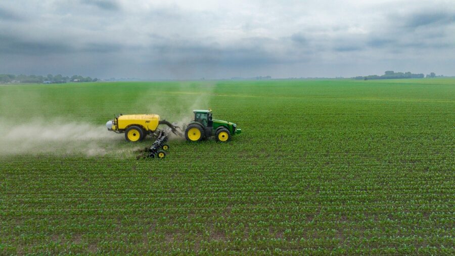 Traktor mit angehaengter Feldspritze faehrt ueber ein Feld mit jungen Pflanzen, Spruehnebel zieht seitlich ab