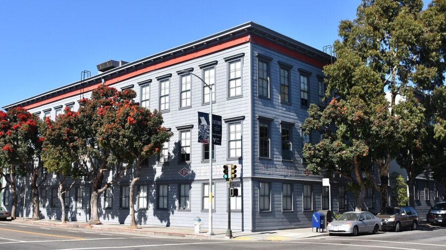Dreistoeckiges graublaues Holzgebaeude an einer Strassenkreuzung in San Francisco mit dem Schriftzug Pioneer Building an der Fassade
