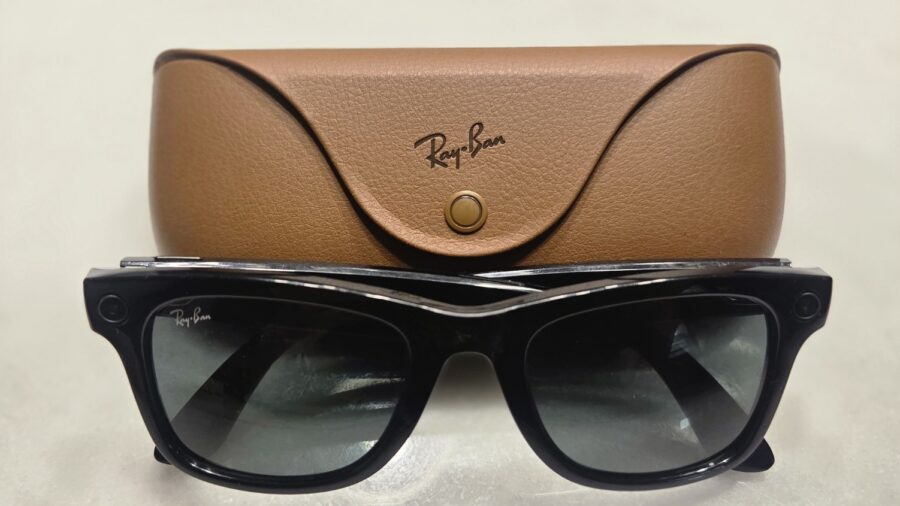 Schwarze Ray-Ban Meta Smart Glasses der ersten Generation vor ihrem braunen Ladeetui, Kameralinse und Aufnahmeleuchte am Rahmen erkennbar