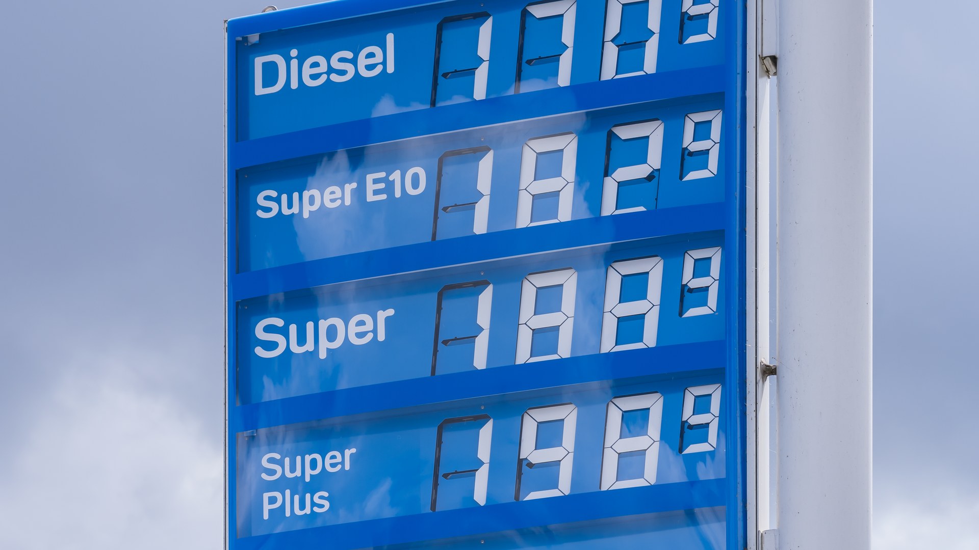 Blaue Preistafel einer Tankstelle vor bewölktem Himmel mit den Zeilen Diesel, Super E10, Super und Super Plus, deren Preisfelder keine Werte anzeigen