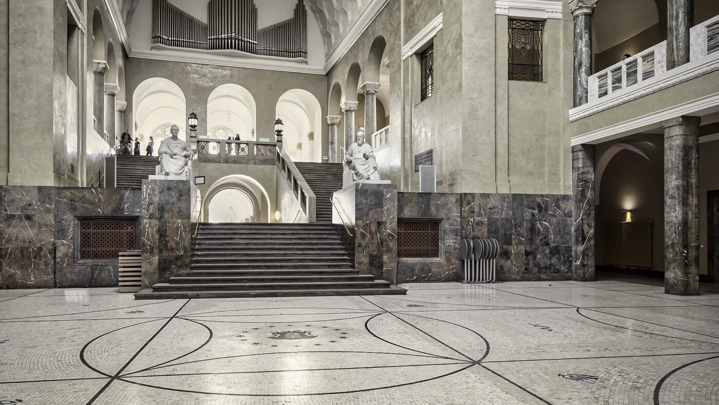 Lichthof mit Marmorsäulen, Treppenaufgang und zwei Sitzstatuen im Hauptgebäude der Ludwig-Maximilians-Universität München