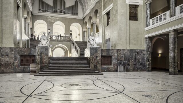 Lichthof mit Marmorsäulen, Treppenaufgang und zwei Sitzstatuen im Hauptgebäude der Ludwig-Maximilians-Universität München