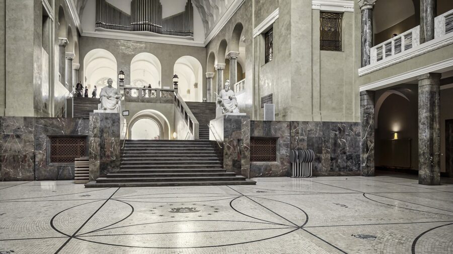 Lichthof mit Marmorsäulen, Treppenaufgang und zwei Sitzstatuen im Hauptgebäude der Ludwig-Maximilians-Universität München