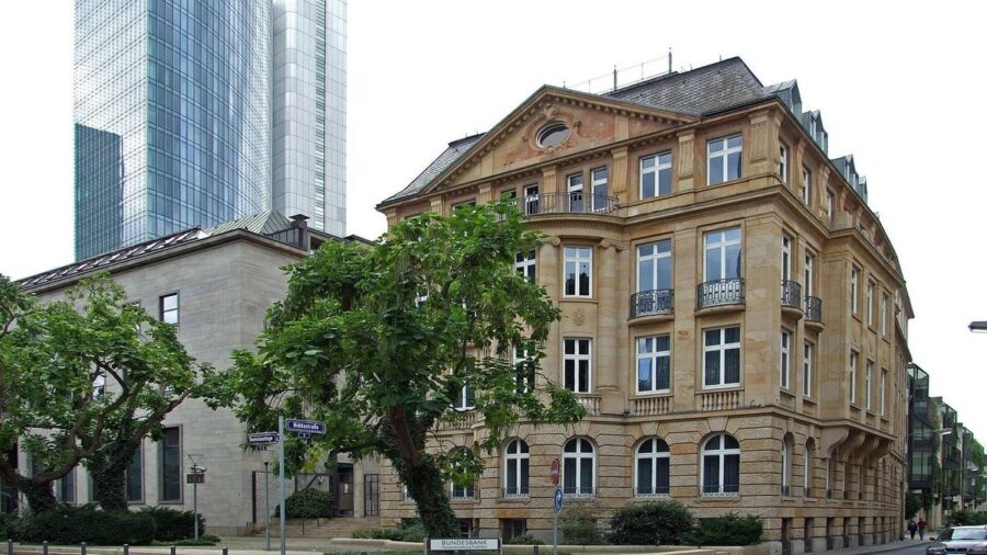 Eckgebäude der Bundesbank-Hauptverwaltung in Frankfurt am Main mit Hinweisschild, dahinter zwei Hochhäuser und Straßenbäume.