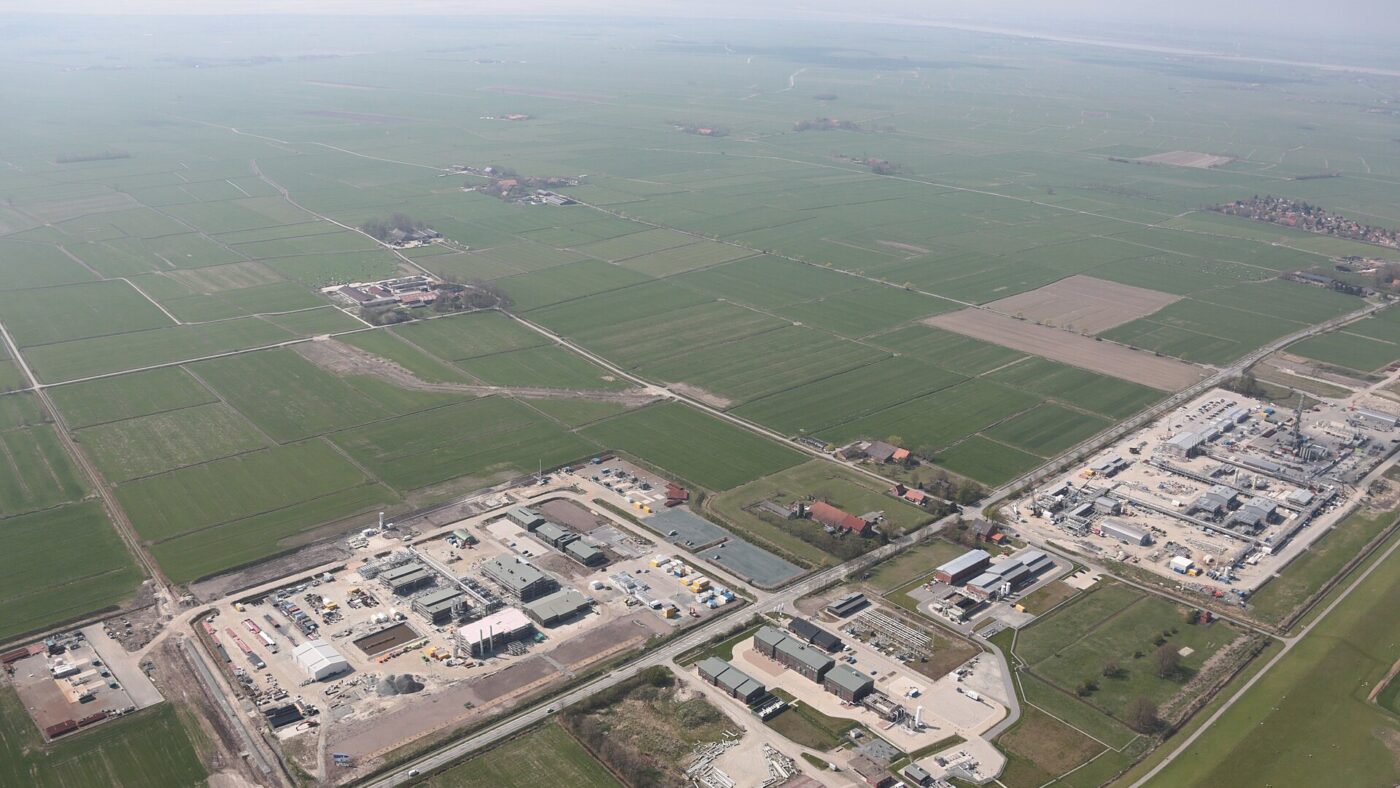 Luftaufnahme von Anlagen der Erdgasinfrastruktur mit Rohrleitungen, Hallen und Betriebsgebäuden inmitten flacher Wiesen und Felder in Nordwestdeutschland