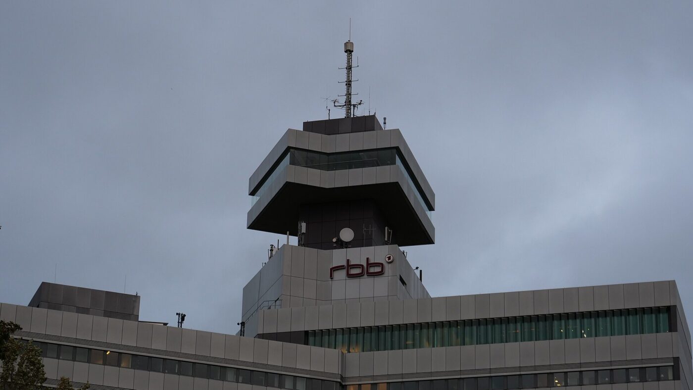 Das Sendezentrum des Rundfunks Berlin-Brandenburg in Berlin mit dem rbb-Schriftzug unterhalb des auskragenden Turmgeschosses, aufgenommen bei bedecktem Himmel.