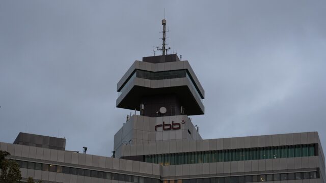 Das Sendezentrum des Rundfunks Berlin-Brandenburg in Berlin mit dem rbb-Schriftzug unterhalb des auskragenden Turmgeschosses, aufgenommen bei bedecktem Himmel.