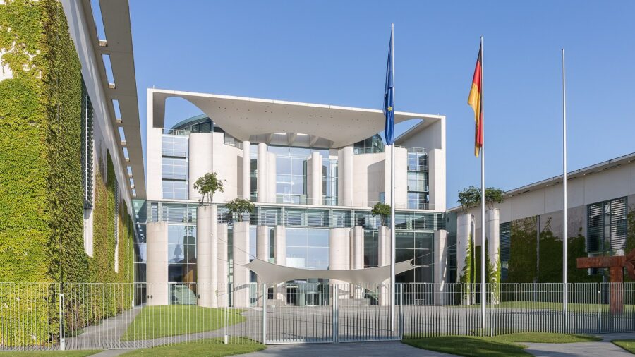 Das Bundeskanzleramt in Berlin bei Sonnenschein, davor die Flaggen Deutschlands und der Europaeischen Union.