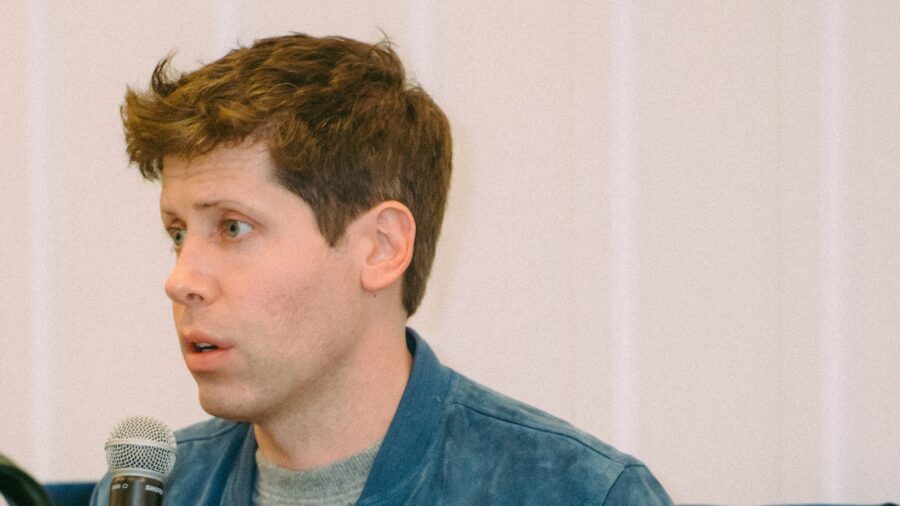 Sam Altman sitzt auf einem Podium und spricht in ein Handmikrofon