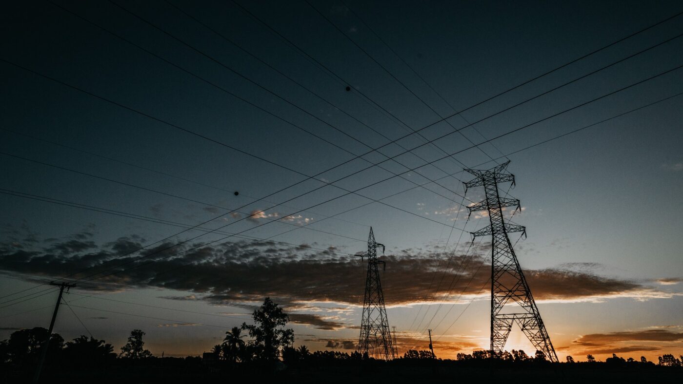 Silhouetten von Hochspannungsmasten und Stromleitungen vor Abendhimmel