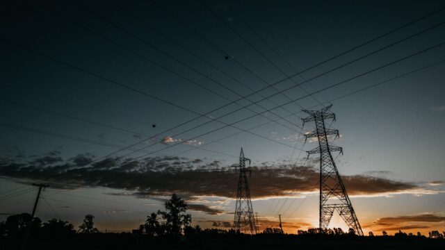 Silhouetten von Hochspannungsmasten und Stromleitungen vor Abendhimmel