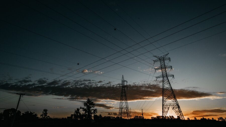 Silhouetten von Hochspannungsmasten und Stromleitungen vor Abendhimmel