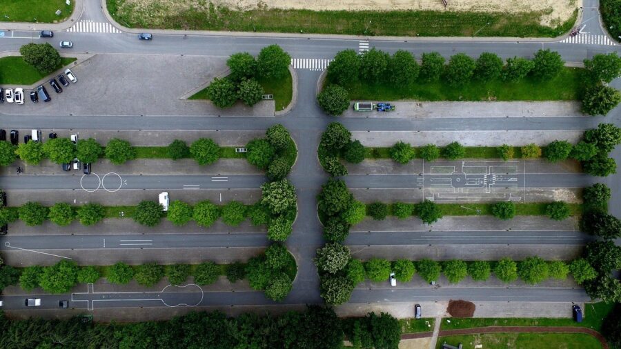 Luftaufnahme eines von Bäumen gesäumten Parkplatzes mit einzelnen abgestellten Autos