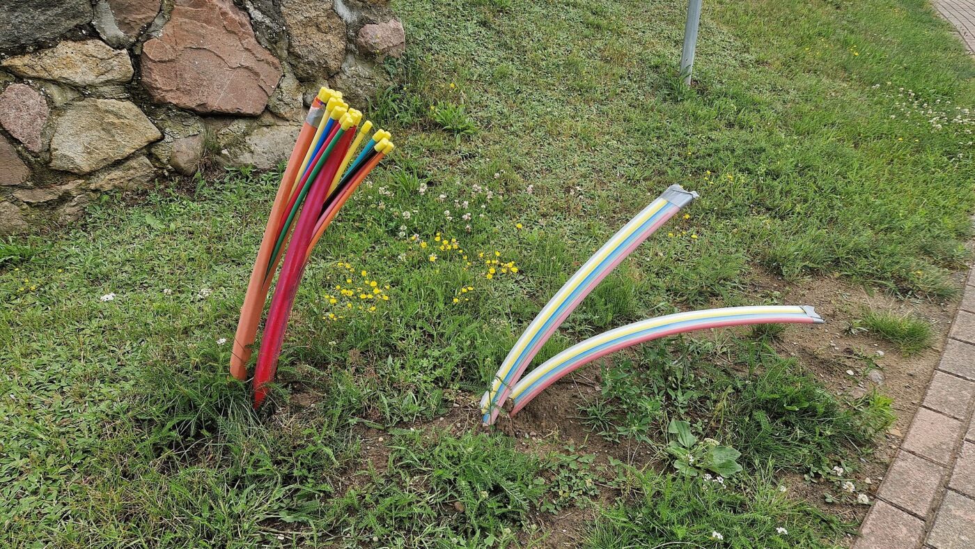Bündel farbiger Leerrohre für Glasfaserkabel ragt neben einer Natursteinmauer aus dem Boden