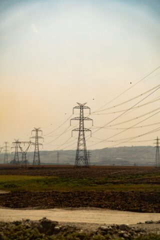 Hochspannungsleitungen und Strommasten in ländlicher Landschaft bei Dämmerung, Symbolbild zu steigenden Strompreisen in Deutschland.